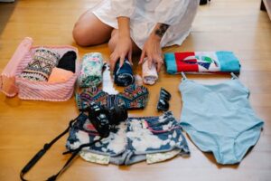Person preparing for beach trip with essentials like clothes, camera, and towel.